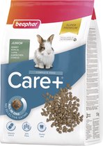 Een bruin-witte jonge konijn kijkt naar de camera, naast een zak beaphar Care+ Junior konijnenvoer.