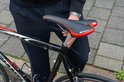 Zwart fietszadel met rode accenten, "SPORT" tekst, gemonteerd op een racefiets.