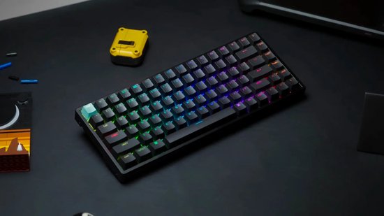 Zwart mechanisch toetsenbord met verlichte toetsen in regenboogkleuren, geplaatst op een bureau naast enkele Lego-onderdelen.