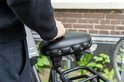 Een persoon met een parelketting raakt een zwart fietszadel aan, met vering.