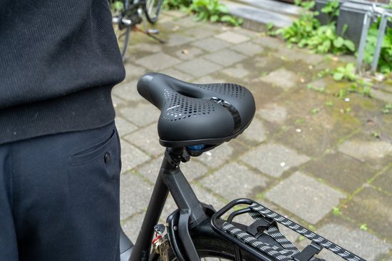 Zwart fietszadel met perforaties en bagagedrager van een fiets, close-up op het zadel.