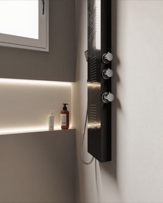 Close-up van een zwarte douchekolom met chromen knoppen en verlichting, naast een nis met zeepdispensers.