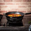 Zwarte Royalty Line koekenpan met marmeren anti-aanbaklaag staat op een gasfornuis en wordt gebruikt om een gerecht met eieren en saus te koken.