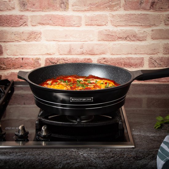 Zwarte Royalty Line koekenpan met marmeren anti-aanbaklaag staat op een gasfornuis en wordt gebruikt om een gerecht met eieren en saus te koken.