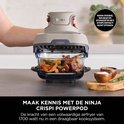 Hand houdt grijze Ninja CRISPi PowerPod vast, met een bak met vlees en aardappelen.