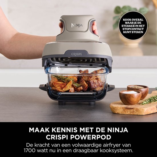 Hand houdt grijze Ninja CRISPi PowerPod vast, met een bak met vlees en aardappelen.