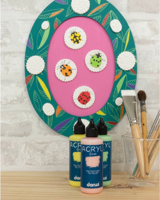 Flesjes gele, roze en groene acrylverf naast schilderborstels en een groene lijst met lieveheersbeestjes.