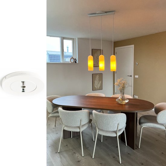 Wit Lightswing ophangsysteem boven een ovale eettafel met stoffen stoelen en gele hanglampen.