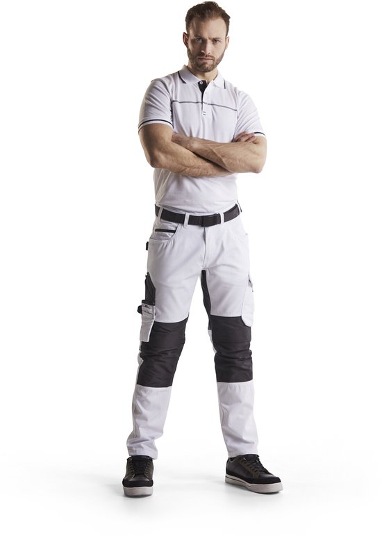 Man in witte polo en werkbroek met witte en zwarte delen, armen gekruist.
