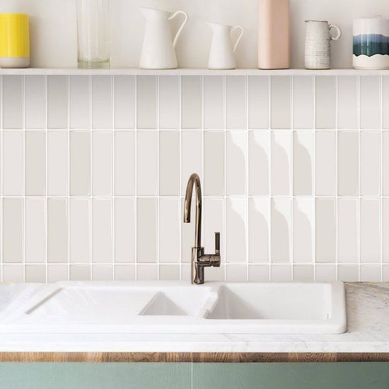 Crème beige glanzende tegels op de achterwand van een keuken met witte spoelbak en koperen kraan.
