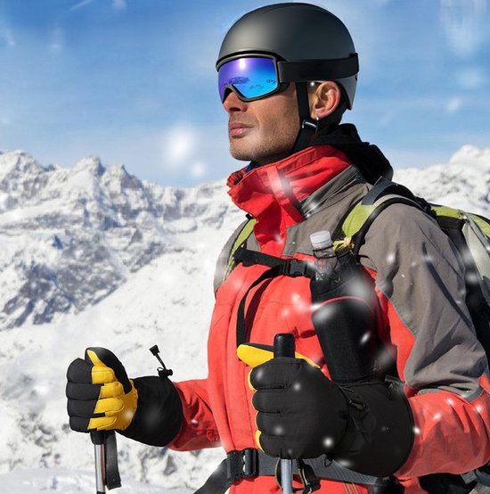 Homme portant un casque de ski, lunettes de ski, veste rouge, gants noirs et jaunes, bâtons de ski dans des montagnes enneigées.