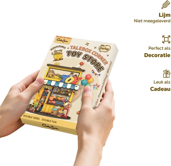 Doos van het modelbouwpakket 'Toy Store Corner' met de speelgoedwinkel erop afgebeeld, vastgehouden door twee handen.
