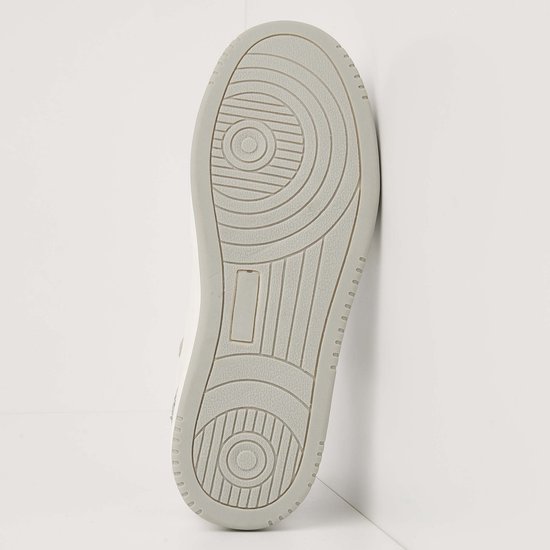Onderkant van een witte sneaker met grijze zool en cirkelvormig profiel.