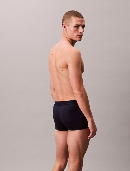 Man met gespierd bovenlichaam in donkerblauwe Calvin Klein boxershort, gedraaid.