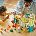 Père et enfant jouant avec une maison Duplo sur une table, avec des jouets Duplo autour.