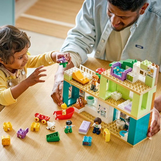 Père et enfant jouant avec une maison Duplo sur une table, avec des jouets Duplo autour.