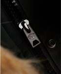 Detailopname van de metalen rits van een donkergroene jas, met het Superdry logo.