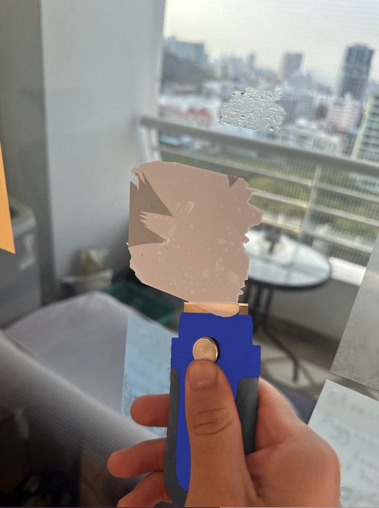 Hand gebruikt blauwe schraper met metalen mes om vuil van een glazen raam te verwijderen.