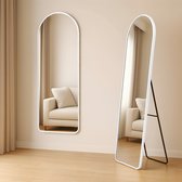 Een witte, afgeronde spiegel met een minimalistisch frame staat op een houten vloer.