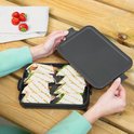 Une femme pose le couvercle sur une boîte à lunch contenant des wraps grillés, avec des fraises en arrière-plan.