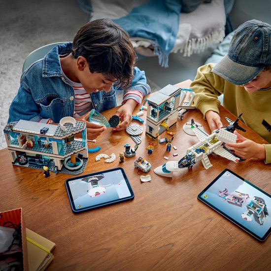 Twee jongens bouwen een LEGO City luchthaven met vliegtuig op een tafel. Een tablet toont instructies.