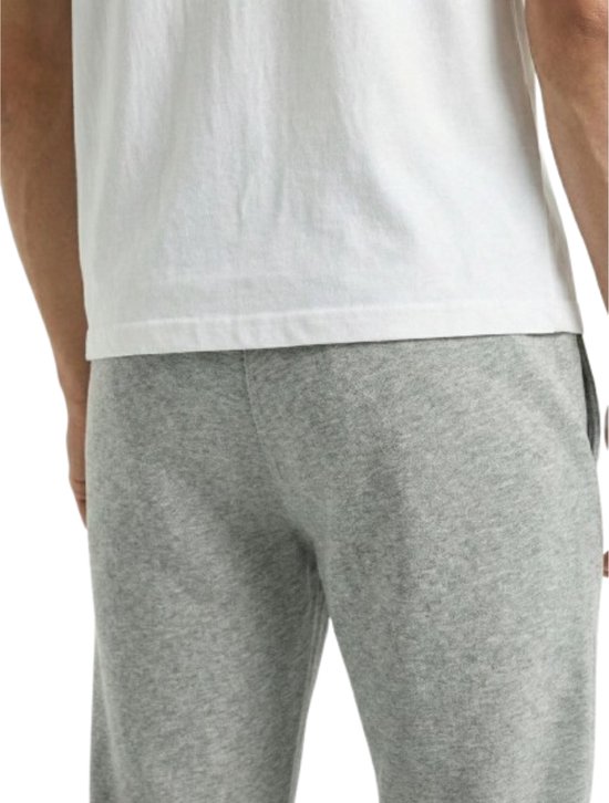 Detail van de heup van een lichtgrijze joggingbroek met een rood detail op de zijkant.