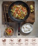 Poêle antiadhésive noire remplie de nouilles, légumes et crevettes, sur une planche à découper en bois.
