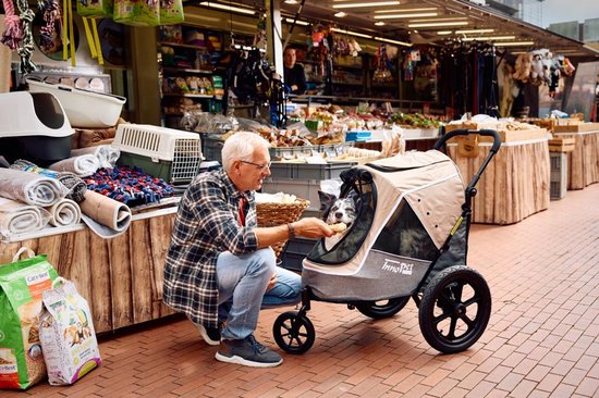 Man voert hond in beige InnoPet buggy op een markt.