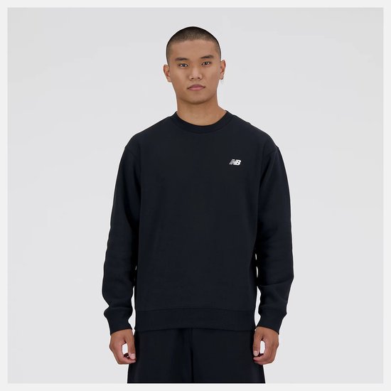 Een man staat met een zwarte New Balance sweater met wit logo op de borst.