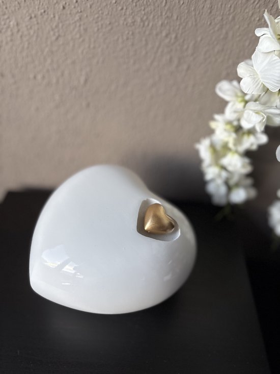 Wit hartvormige urn met een gouden hartje, naast witte bloemen.