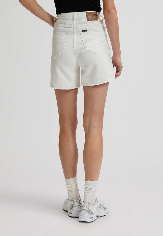 Zijzicht van een vrouw in een witte spijkerbroekshort met wijde pijpen, achterkant zichtbaar.