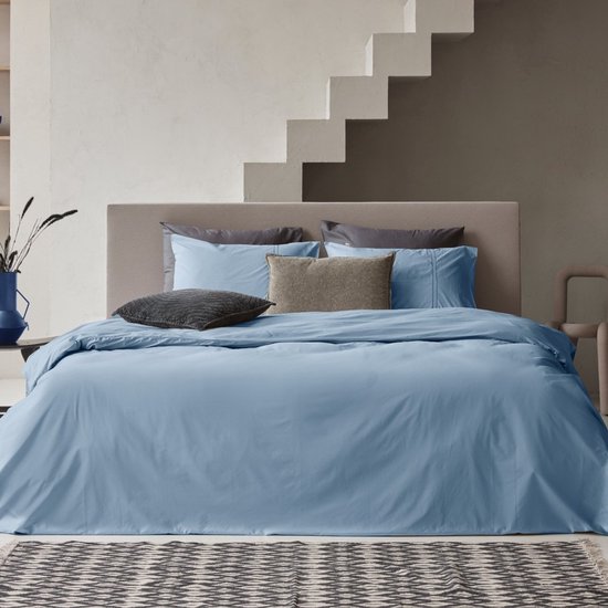Un lit entièrement fait avec une housse de couette bleu clair et divers oreillers.