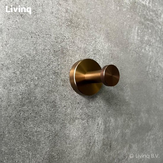 Bronzen handdoekhaak met ronde basis, gemonteerd op een grijze muur.