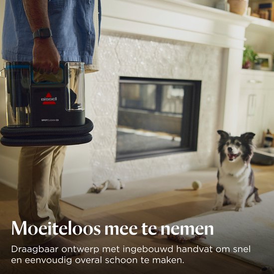 Man draagt de BISSELL SpotClean C5 bij een open haard, naast een hond. "Moeiteloos mee te nemen".