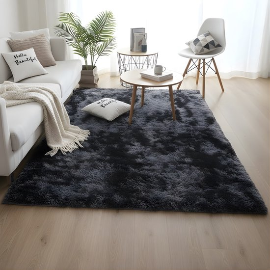 Donkergrijs, hoogpolig vloerkleed in een lichte woonkamer met een witte bank, salontafel en planten.