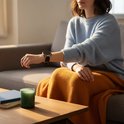 Femme en pull bleu et plaid orange portant une montre connectée avec bracelet en métal noir.