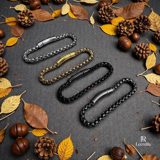 Vier schakelarmbanden in zilver, goud, zwart en grijs, met karabijnsluitingen, te midden van herfstbladeren en dennenappels.