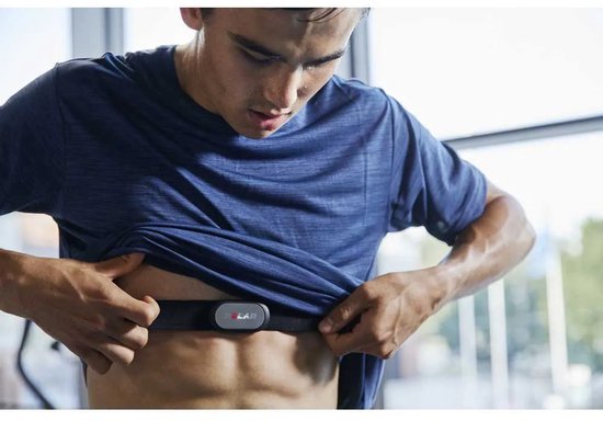 Man met spierbuik draagt een zwarte Polar hartslagsensor op zijn borst, trekt shirt omhoog.