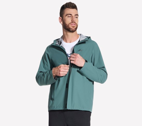 Man met groene Skechers regenjas, ritst de jas dicht.