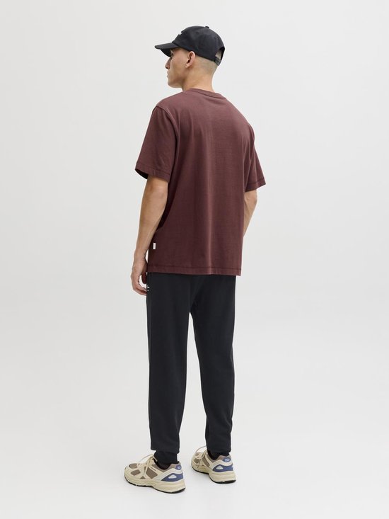 Man met de rug naar de camera, draagt een donkerrode T-shirt en zwarte joggingbroek met witte opdruk.
