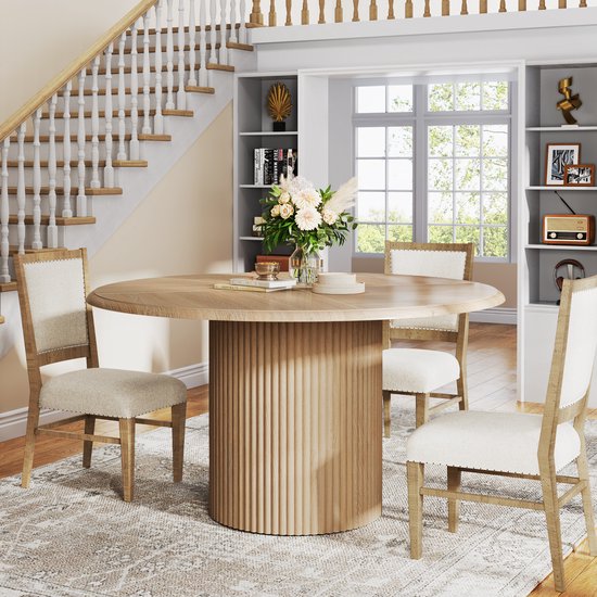 Ronde eettafel met houten visgraatblad en gecanneleerde poot, in een woonkamer met een trap en open kasten.