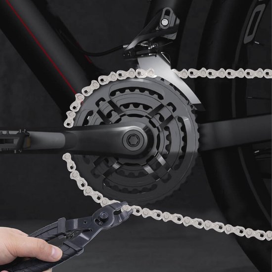 Hand met tang die aan een fietsketting werkt, dichtbij een tandwiel van een zwarte fiets.