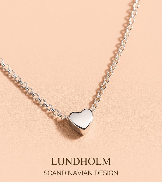 Collier argenté avec un pendentif en forme de cœur sur fond rose pâle. Lundholm Design Scandinave.