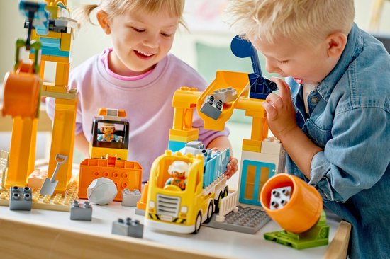 Twee kinderen spelen met geel bouwspeelgoed met een kraan en vrachtwagen.