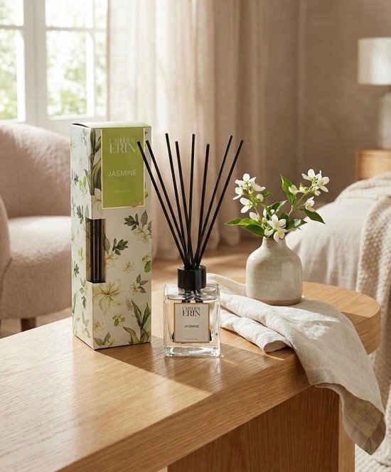 L'Atelier Erin Jasmijn reed diffuser met zwarte stokjes, naast een vaas met jasmijnbloesems.
