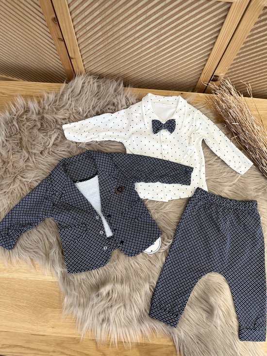 Losse delen van een baby outfit: donkerblauwe blazer, broek en wit poloshirt met stippen en strikje.