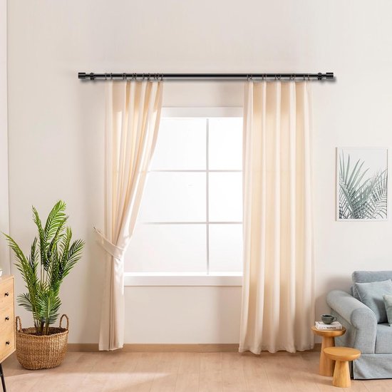 Een zwarte, uitschuifbare gordijnroede hangt boven een raam met beige gordijnen.