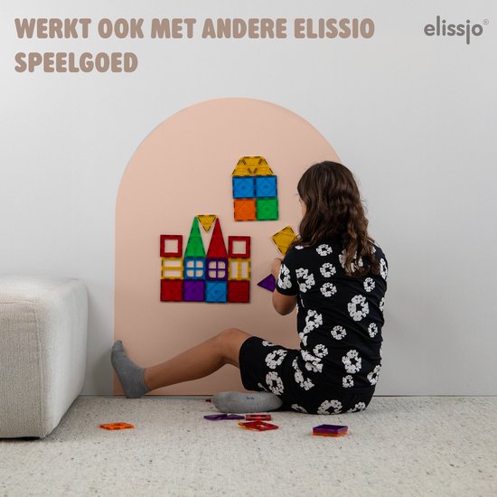 Meisje zit op de grond en bouwt met magnetische bouwstenen op een boogvormige muursticker. De bouwstenen zijn geel, blauw, groen, rood, paars, oranje en transparant.