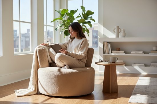 Vrouw leest boek in zachte, taupe fauteuil met een gebogen rugleuning. Een plaid hangt over de armleuning.