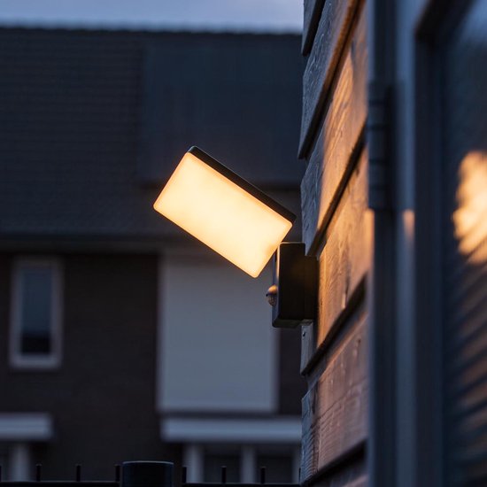 Zwarte wandlamp met sensor, verlicht de houten schutting 's avonds.
